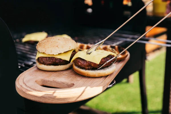 Serving tongs holding hot burgers grilled for outdoors barbecue — Stock Photo