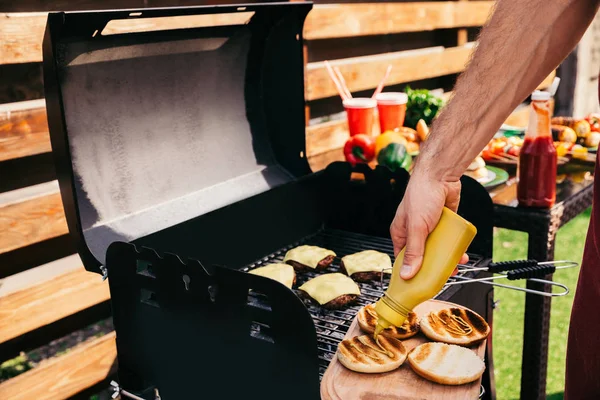 Chef adding mustard to burgers grilled for outdoors barbecue — Stock Photo