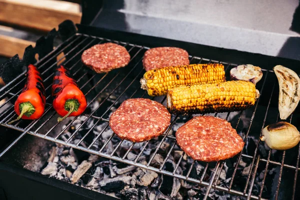 Meat patties and vegetables cooked outdoors on grill — Stock Photo
