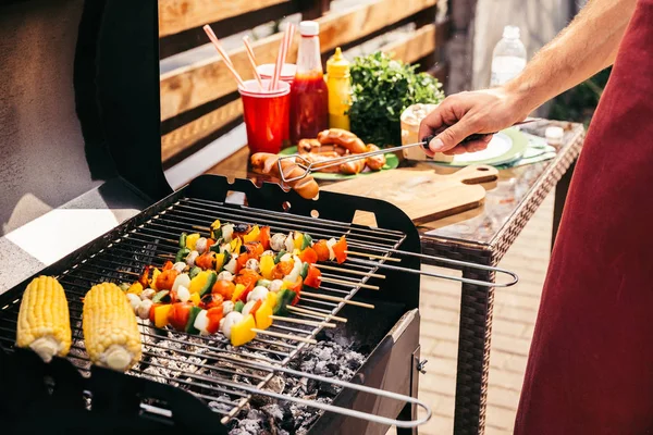Man checking vegetables and sausages grilled for outdoors barbecue — Stock Photo