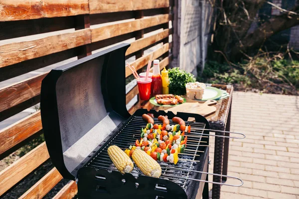 Seasonal vegetables and sausages cooked outdoors on grill — Stock Photo