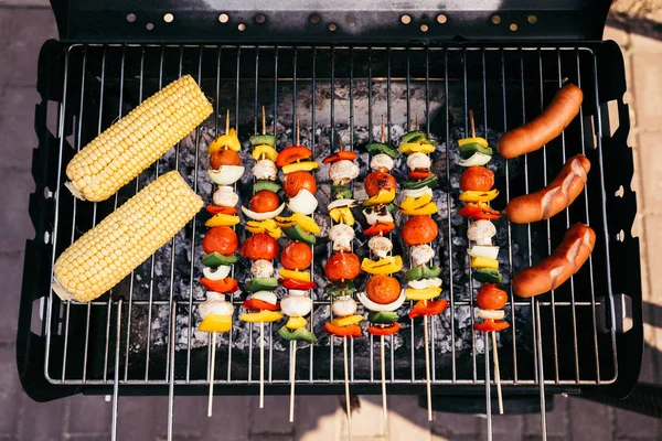 Sausages cooked outdoors on grill with corn and vegetables — Stock Photo