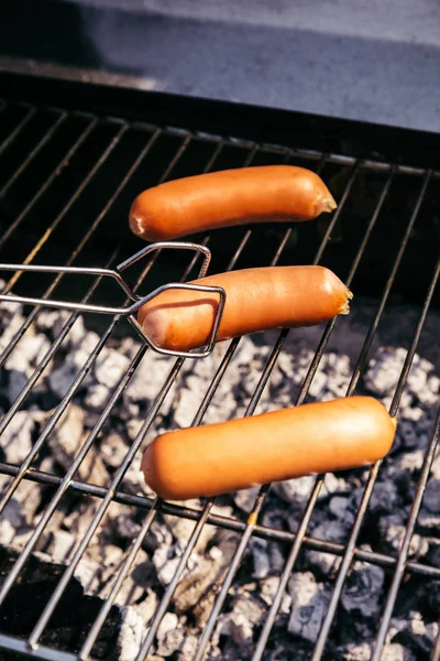 Serving tongs adjusting sausages grilled for outdoors barbecue — Stock Photo