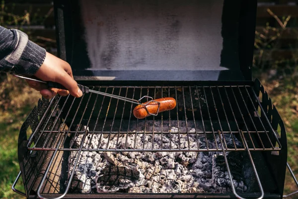 Man with serving tongs cooking sausages outdoors on grill — Stock Photo