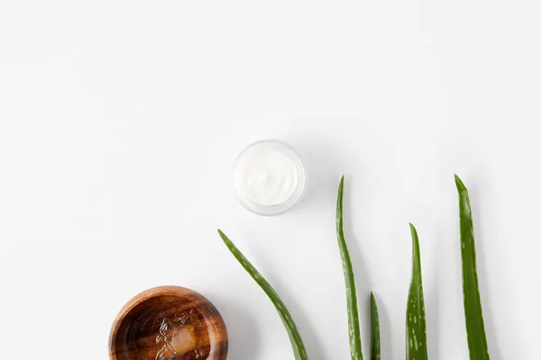 Vue du dessus d'un bol en bois avec jus d'aloe vera, crème biologique en récipient et feuilles d'aloe vera sur surface blanche — Photo de stock