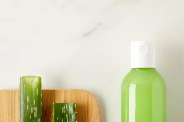 Elevated view of aloe vera leaves on cutting board and organic shower gel in bottle on marble table — Stock Photo