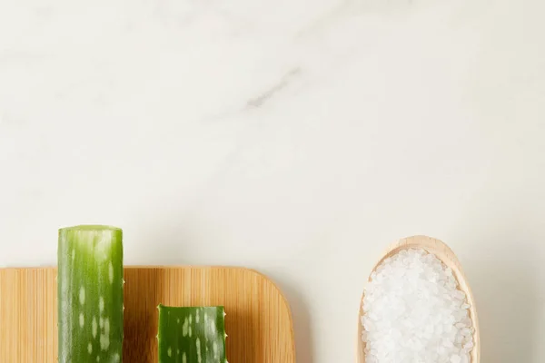 Elevated view of aloe vera leaves on cutting board and wooden spoon with salt on marble table — Stock Photo