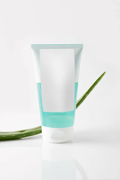 Vista close-up de tubo de creme e folha de aloe vera na superfície branca — Fotografia de Stock