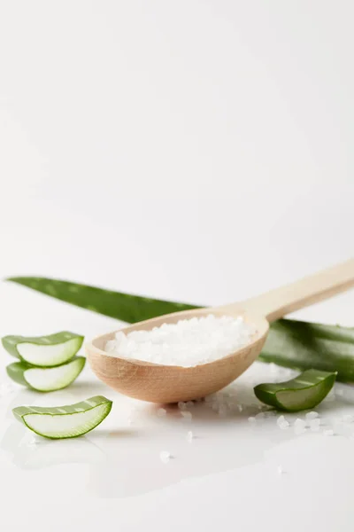 Immagine ravvicinata di cucchiaio di legno con sale, foglia di aloe vera e fette su superficie bianca — Foto stock