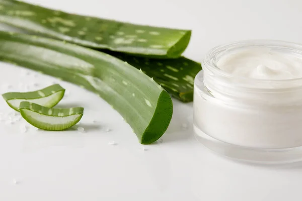 Closeup view of organic cream in container, aloe vera leaves and slices on white surface with salt — Stock Photo