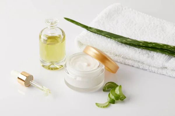 Crema biologica e profumo, pipetta, asciugamani e fette di aloe vera e foglia su superficie bianca — Foto stock