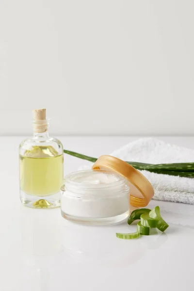 Close up shot of organic cream and perfume, towel and aloe vera slices and leaf on white surface — Stock Photo