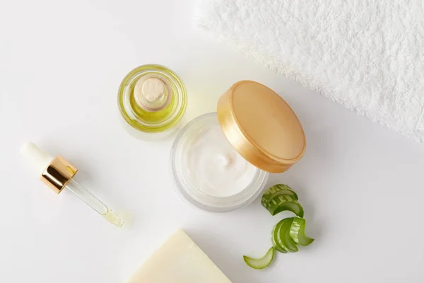 Vista superior de creme orgânico, óleo cosmético e sabão, pipeta, toalha e fatias de aloe vera na superfície branca — Fotografia de Stock