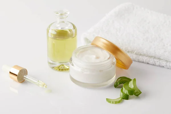 Closeup shot of organic oil and cream, dropper, towel and aloe vera slices — Stock Photo
