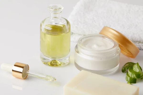 Closeup shot of cosmetic oil, dropper, soap, towel, organic cream in container and aloe vera slices — Stock Photo