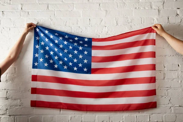 Cropped image of man and woman holding american flag against brick wall — Stock Photo