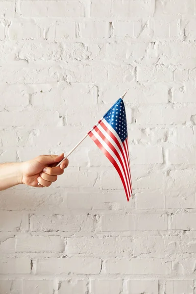 Imagem cortada do homem segurando bandeira americana contra parede de tijolo branco — Fotografia de Stock