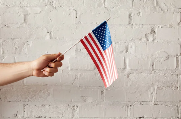 Частичный вид человека, держащего американский флагшток на стене из белого кирпича — стоковое фото