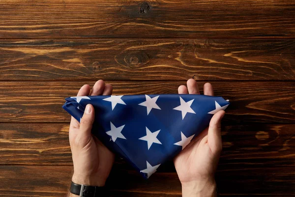 Corte tiro de homem segurando dobrado bandeira americana no fundo de madeira — Fotografia de Stock