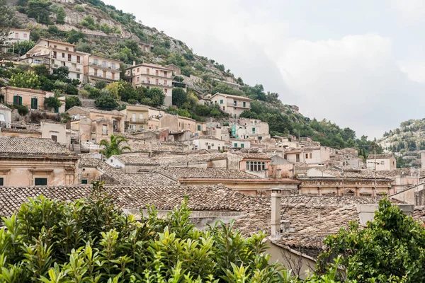 Pequeñas casas en la colina cerca de plantas verdes en modica, italia - foto de stock