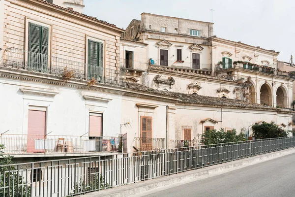 Green trees near fence and old buildings in modica, Italy — Stock Photo