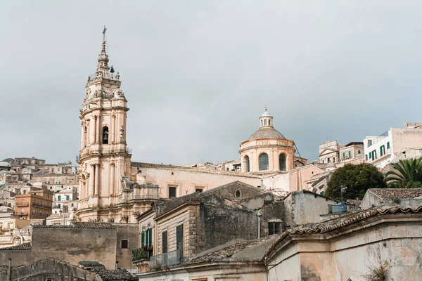 MODICA, ITALIA - 3 OTTOBRE 2019: Cattedrale barocca di San giorgio vicino a case contro il cielo con nuvole in Sicilia — Foto stock