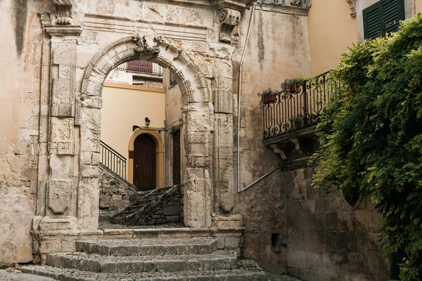 Древняя арка в старом здании рядом с зелеными растениями в modica, Италия — стоковое фото