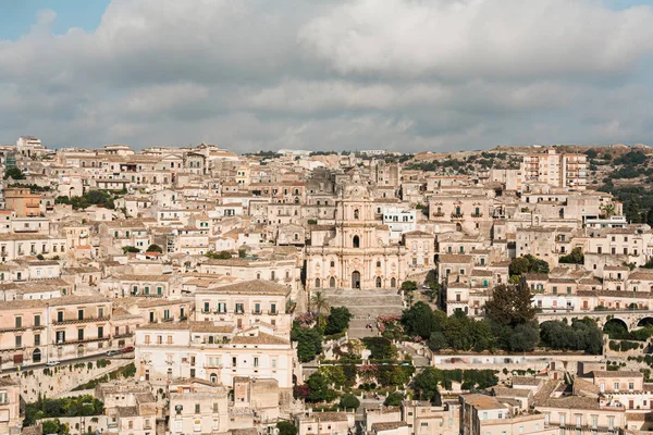 MODICA, ITALIE - 3 OCTOBRE 2019 : Cathédrale baroque de san giorgio près de vieilles maisons contre le ciel avec des nuages — Photo de stock