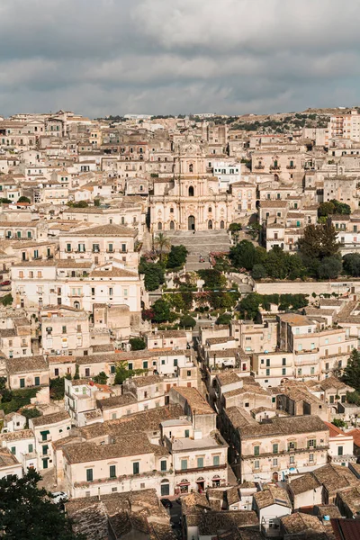 Modica, italien - 3. oktober 2019: barocke kathedrale von san giorgio in der nähe von häusern und grünen bäumen — Stockfoto