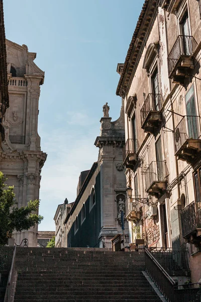 CATANIA, ITALIA - 3 DE OCTUBRE DE 2019: vista en ángulo bajo de la fachada de la catedral de Catania cerca de escaleras y casas - foto de stock