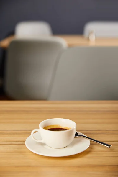 Selective focus of white cup of coffee near spoon in cafe — Stock Photo