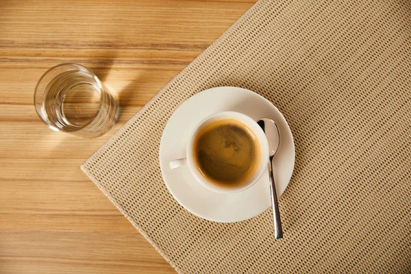 Вид сверху чашки с горячим кофе рядом со стеклом с водой в кафе — стоковое фото