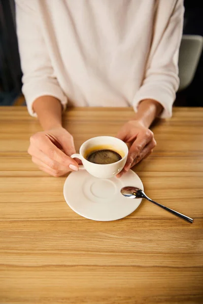 Обрезанный вид женщины, держащей чашку кофе в кафе — стоковое фото