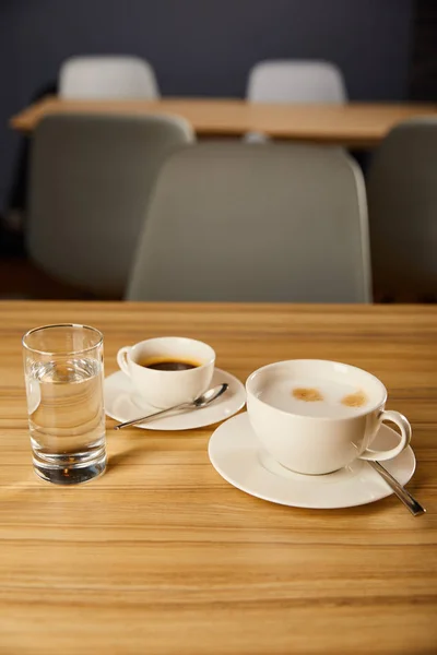 Enfoque selectivo de tazas con café cerca de vaso de agua en la cafetería - foto de stock