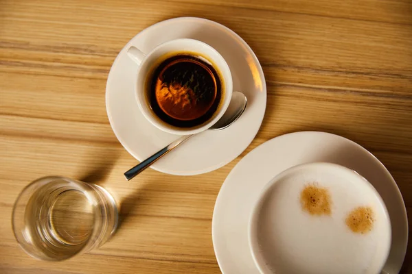 Vista superior de tazas con café cerca de vaso de agua en la cafetería - foto de stock