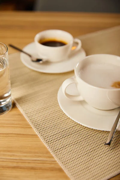 Foco seletivo de café quente em copos perto de vidro de água — Fotografia de Stock