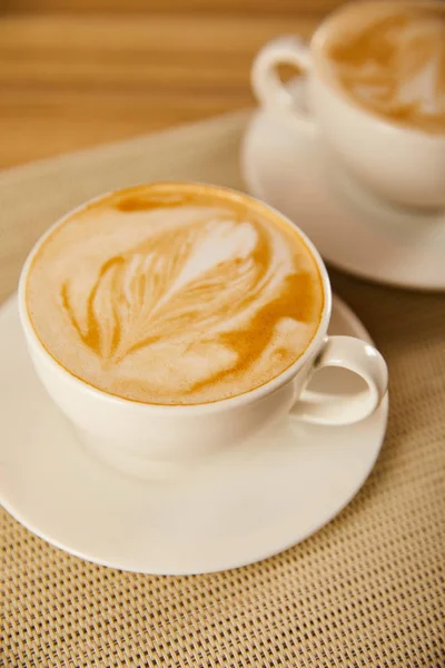 Foco seletivo de cappuccino saboroso em copos brancos na mesa — Fotografia de Stock