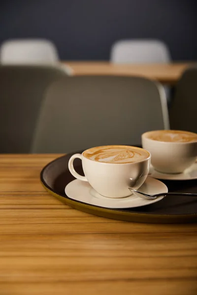 Messa a fuoco selettiva del cappuccino in tazze bianche su vassoio nero — Foto stock