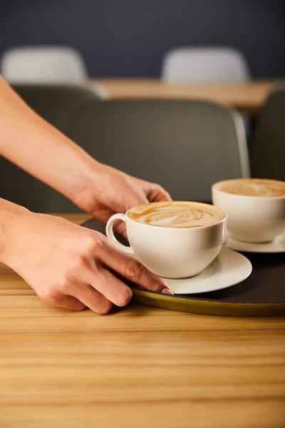 Cropped view of woman holding saucer with cup of cappuccino — Stock Photo