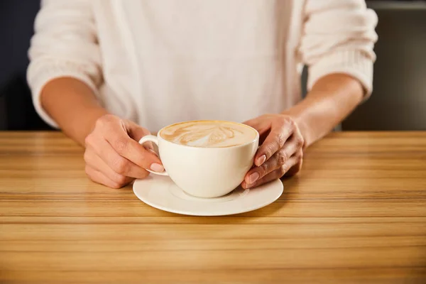 Cropped view of woman holding cup of cappuccino — Stock Photo