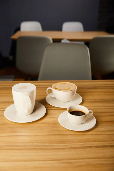 Fuoco selettivo di caffè saporito in tazze bianche su tavolo di legno — Foto stock
