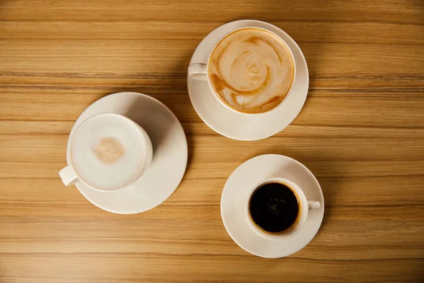 Vista superior de los platillos con tazas blancas de sabroso café en la cafetería - foto de stock