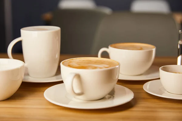 Foco seletivo de pires com xícaras brancas de café saboroso no café — Fotografia de Stock
