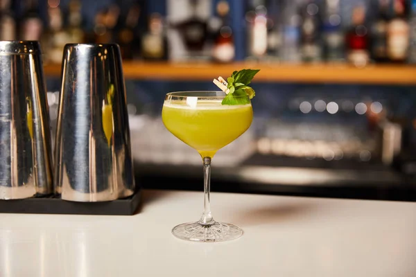 Стакан со свежим алкогольным коктейлем возле шейкера на барной стойке — стоковое фото