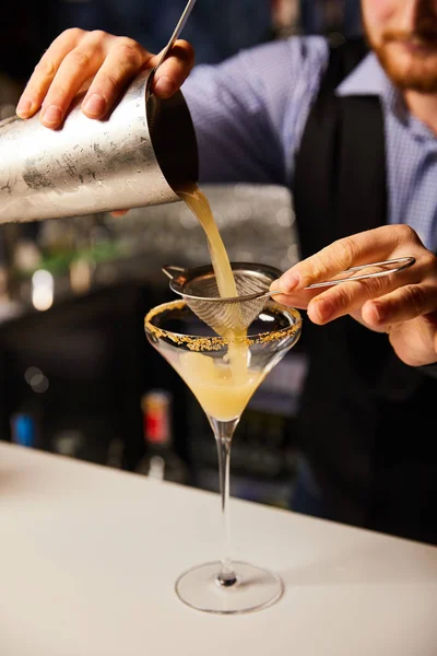 Ausgeschnittene Ansicht eines bärtigen Barmanns, der Cocktails einschenkt, während er einen Shaker in der Nähe von Sieb und Margaritenglas hält — Stockfoto