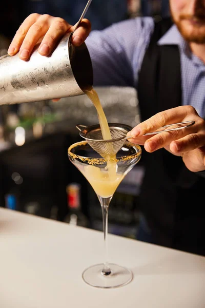 Vista cortada de barman barbudo derramando coquetel enquanto segurando agitador perto da peneira e vidro margarita — Fotografia de Stock