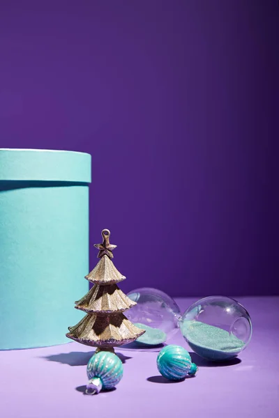 Голубая подарочная коробка и декоративная елка с безделушками и песочными часами на фиолетовом фоне — стоковое фото