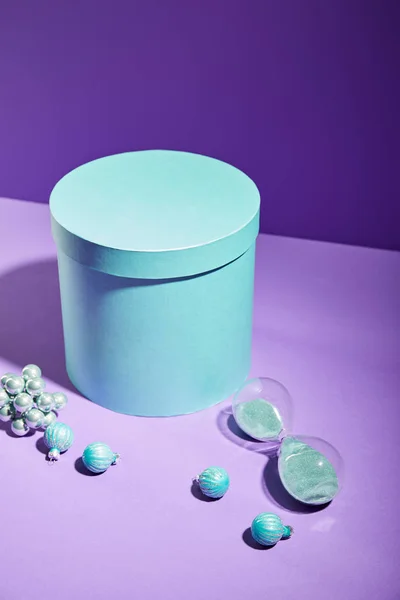 Caixa de presente azul e bugigangas decorativas e ampulheta no fundo roxo — Fotografia de Stock