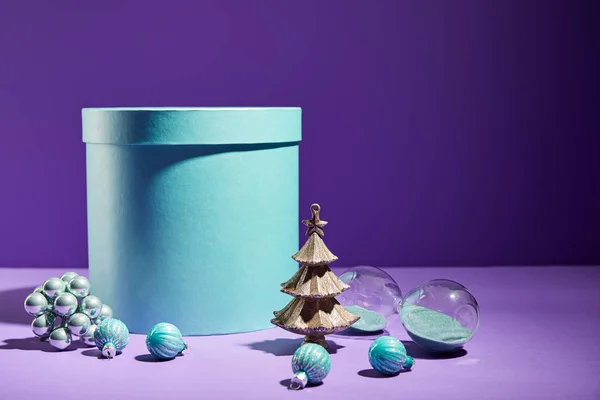 Scatola regalo blu e albero di Natale decorativo con bagattelle su sfondo viola — Foto stock