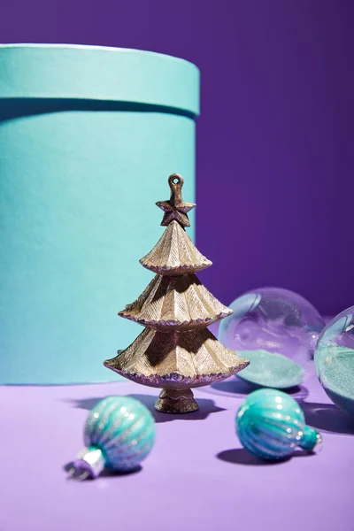 Selective focus of decorative Christmas tree with baubles near hourglass and blue gift box on purple background — Stock Photo
